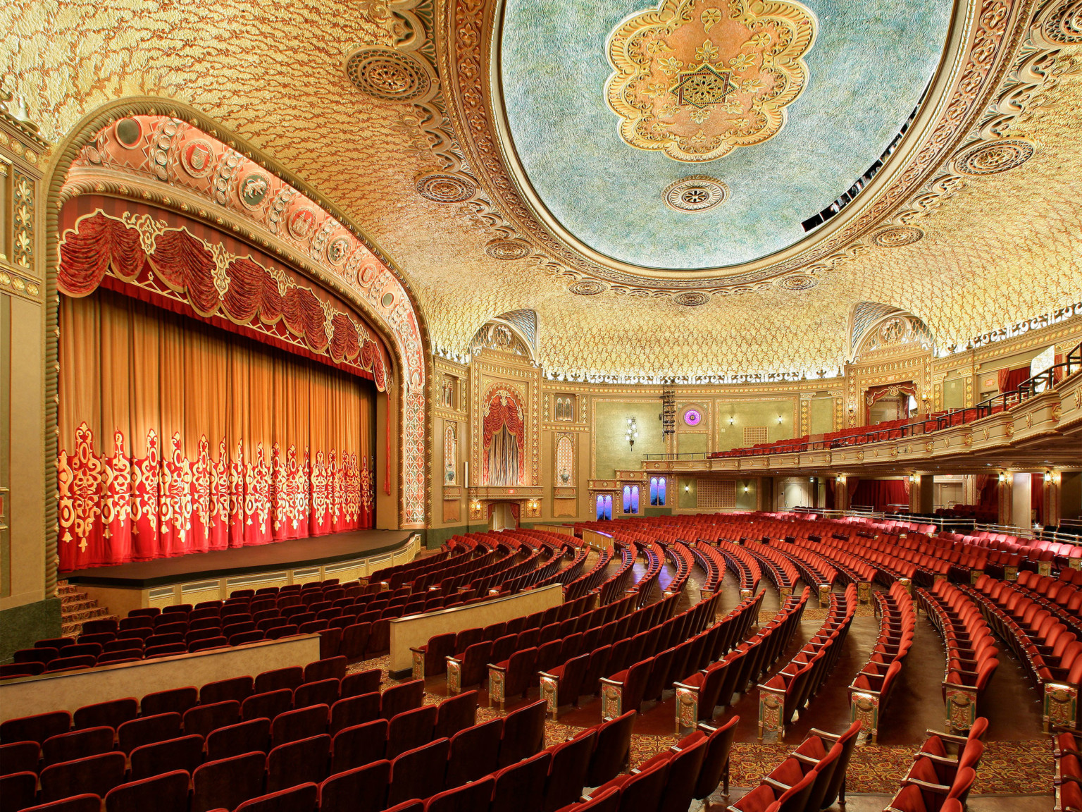 Historic grand theater with red seating, grand ornate archway over stage, red drop curtain, and gold ceiling at the Tennessee Theater