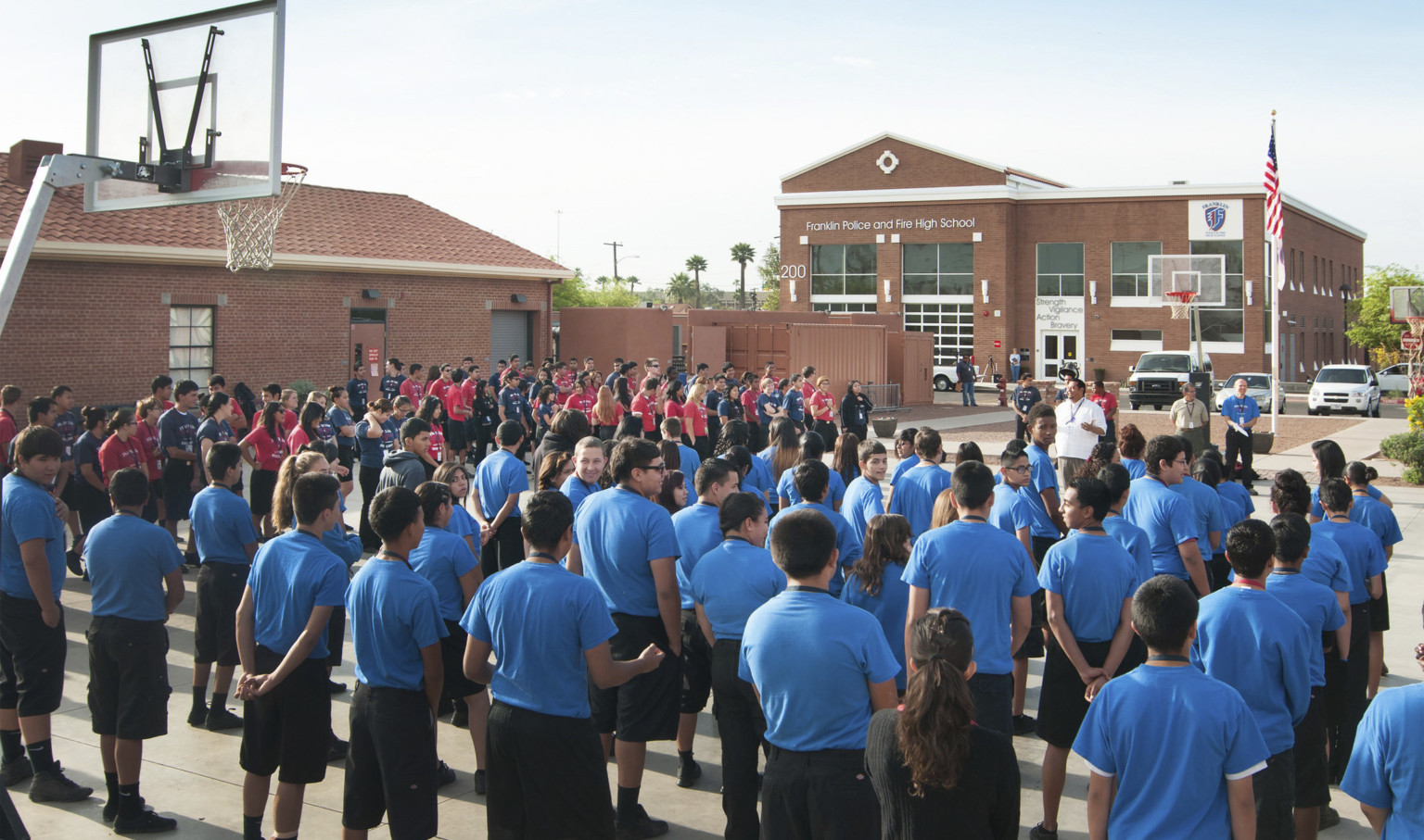 students in an assembly outside on the basketball courts in front of Franklin Police and Fire High School, 2 brick buildings