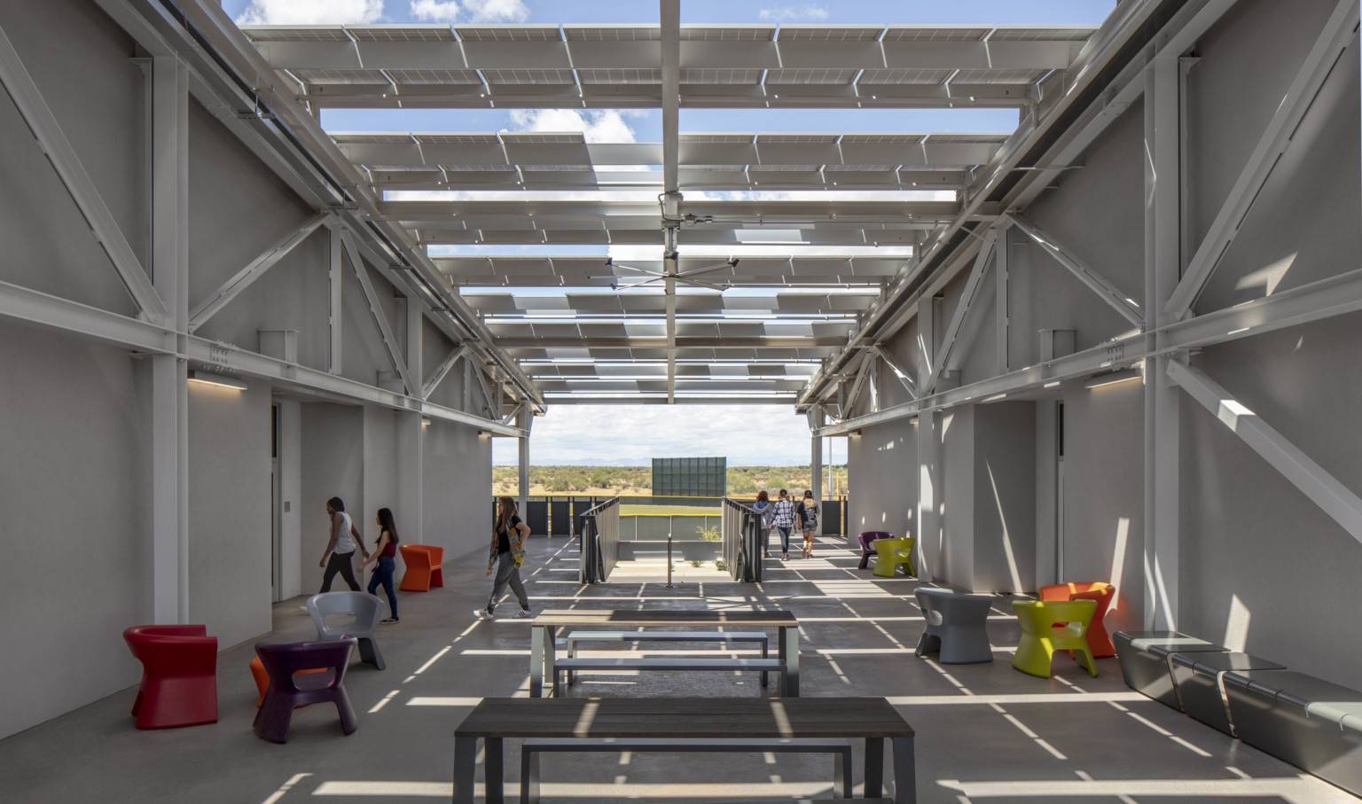 Solar panels stretch in rows between two white buildings, partially covering seating areas Solar panels stretch in rows between two white buildings, partially covering seating areas