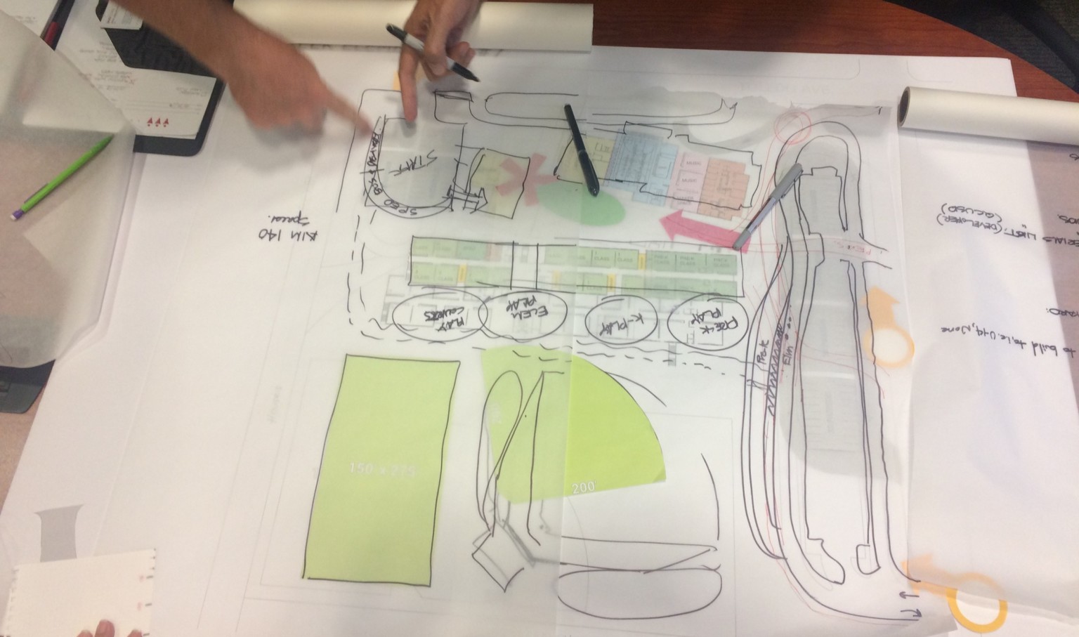 2 people working on a hand drawn rendering, each pointing to the same point in the top left of the photo 2 people working on a hand drawn rendering, each pointing to the same point in the top left of the photo