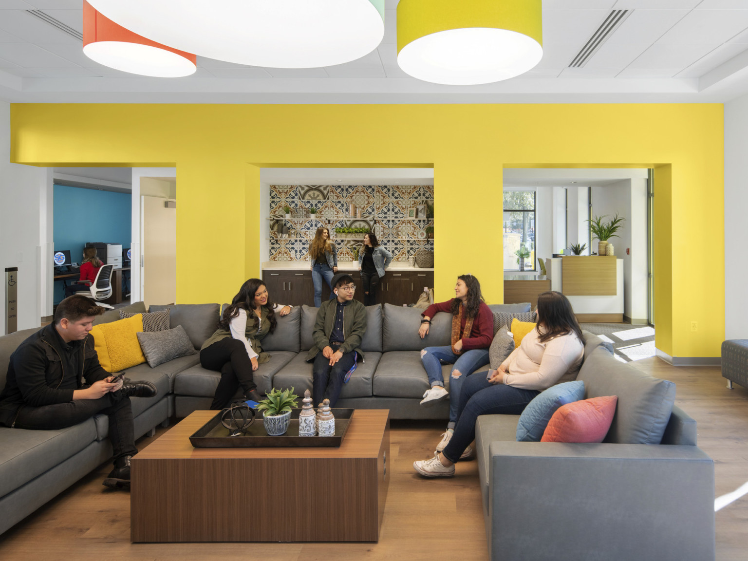 Yellow seating area off entry with large U shaped sectional and coffee table. Recessed counter in center of wall with tiles