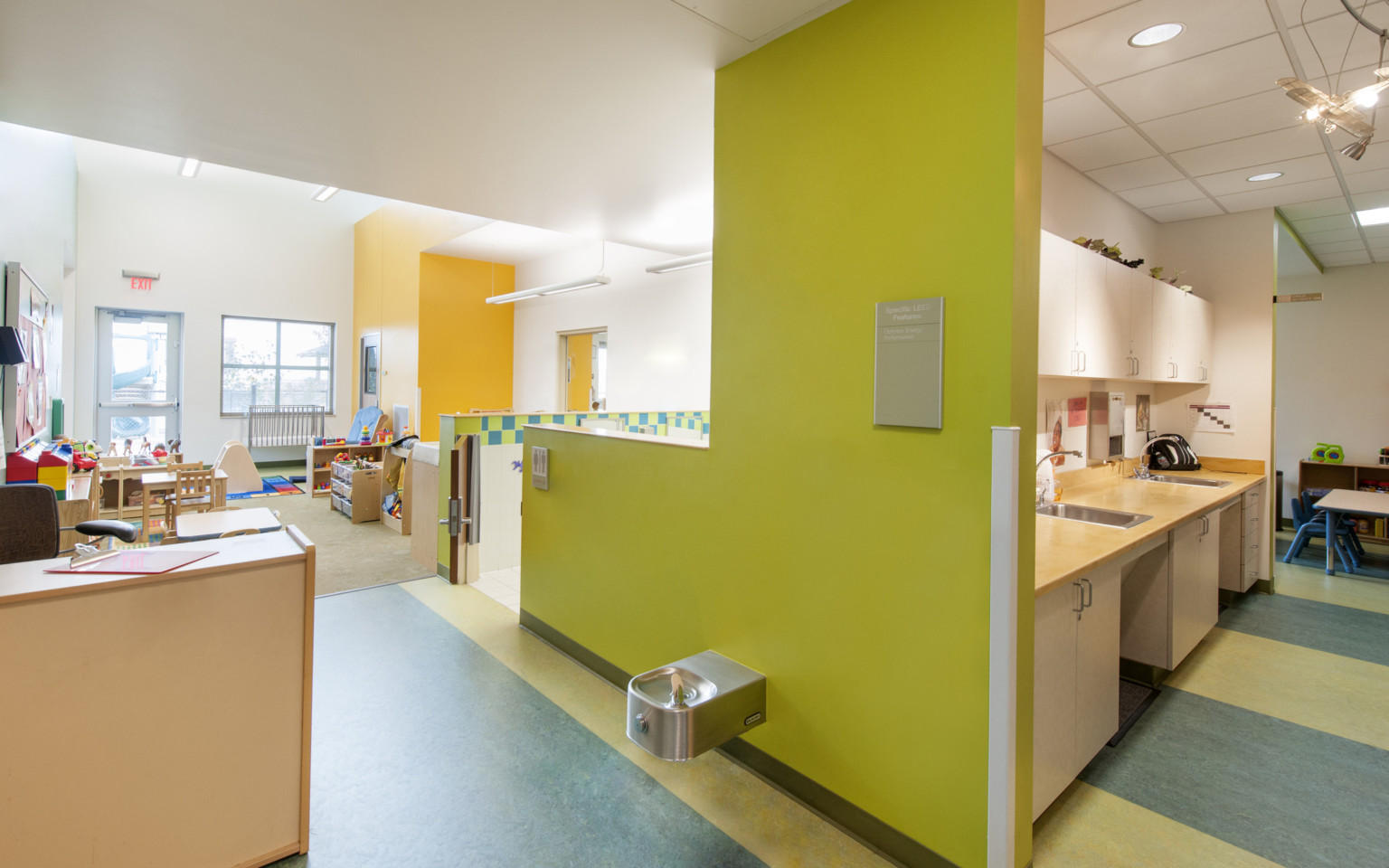 young children's classroom with blue and green flooring, white ceilings, yellow and chartreuse accent walls, and light wood