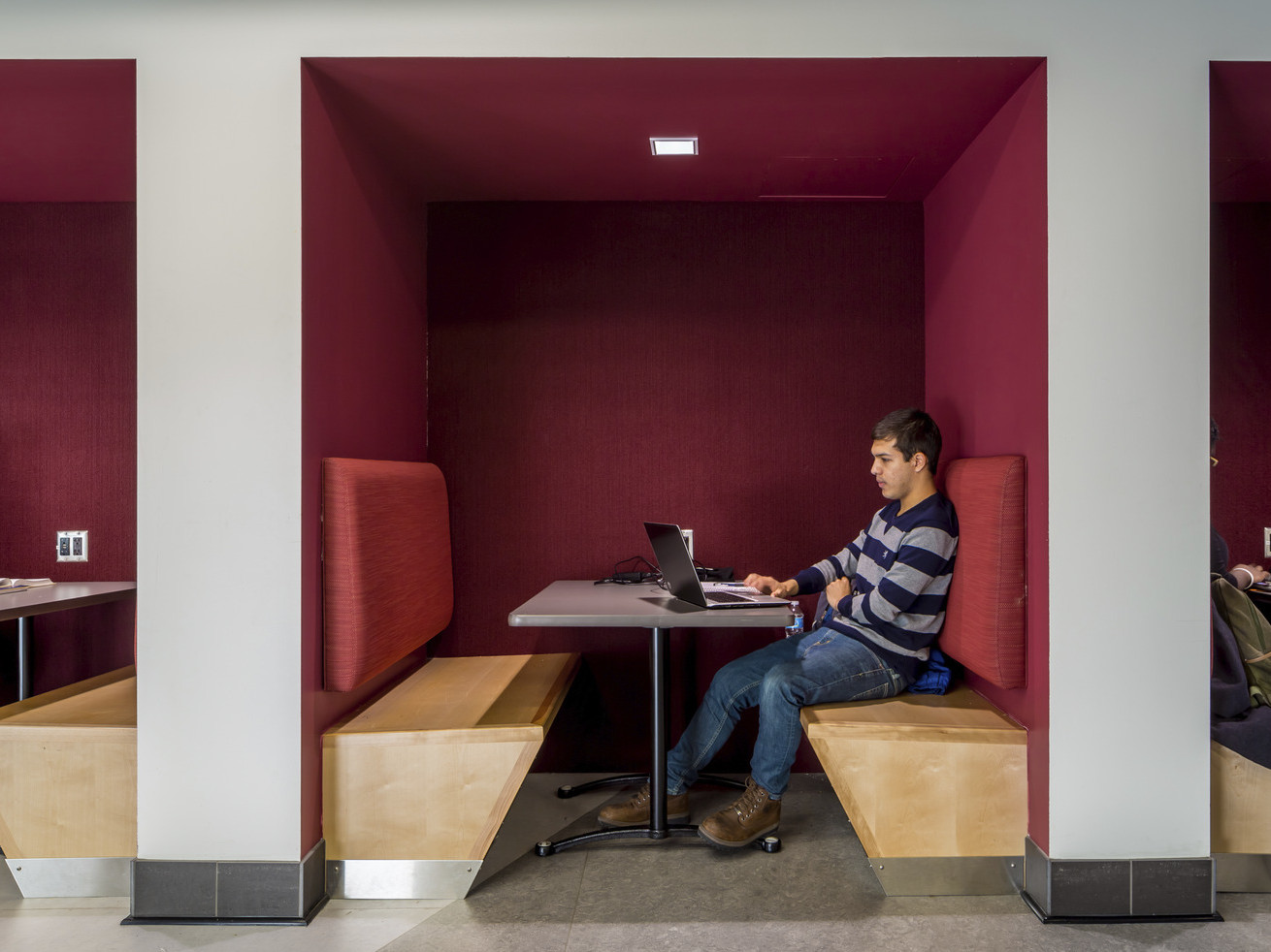 Tucked-in booths for collaboration with wood benches and dark red accents at the University of Minnesota cultural center