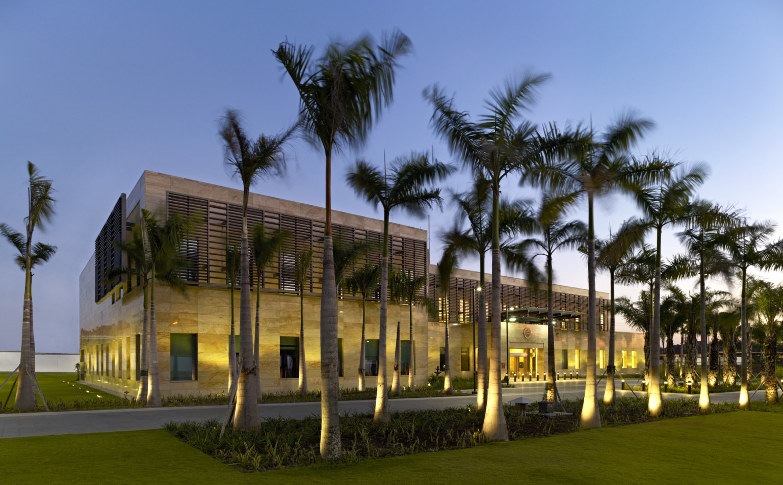 a stone building with brise soleil panels on second story windows. uplights illuminate ground floor, windows, and palm trees a stone building with brise soleil panels on second story windows. uplights illuminate ground floor, windows, and palm trees