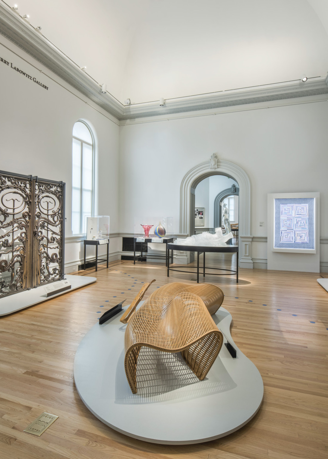a sculptural bench on display in grey gallery with white vaulted roof and arching doorway opposite