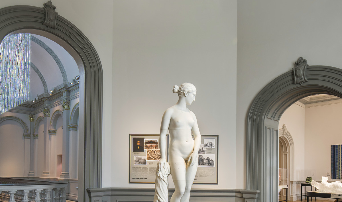 Sculpture of a woman stands on a podium in the center of rotunda with arching molded grey doors