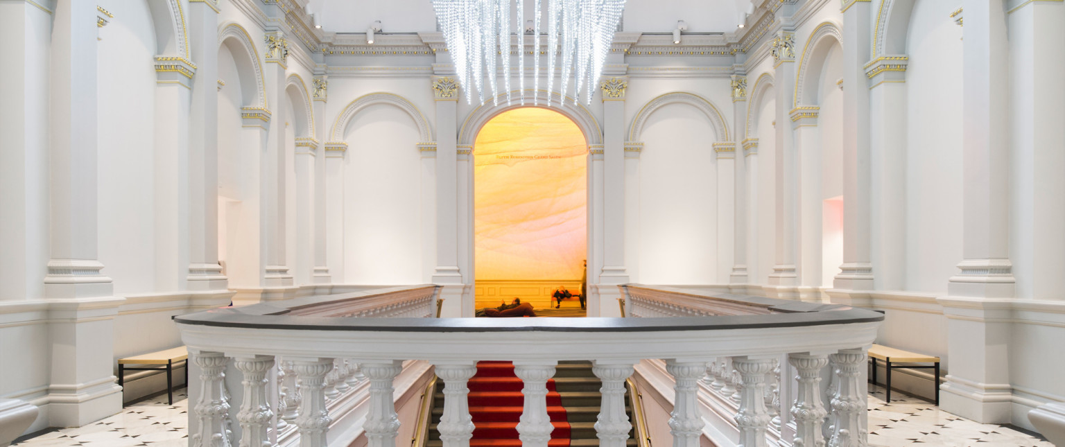Custom sculptural chandelier hanging above staircase in white room at Renwick Gallery, banister with dark accent in front