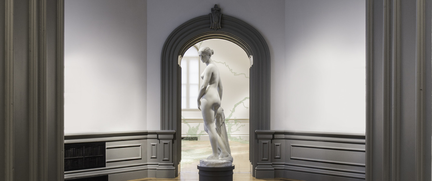 Marble sculpture of a woman on a black pedestal in the center of a small room, framed in front and behind by molded door frame