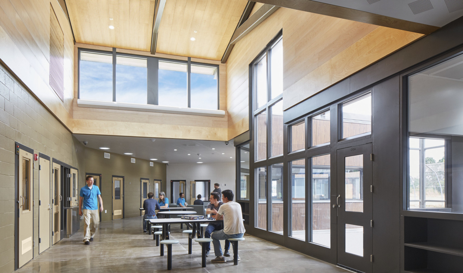 Oregon Youth Authority Maclaren Campus entry hallway. Black framed double height windows at entrance and wood upper walls Oregon Youth Authority Maclaren Campus entry hallway. Black framed double height windows at entrance and wood upper walls