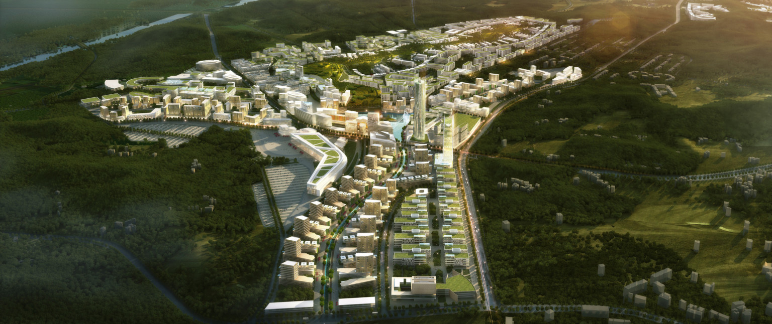 Aerial view of city with green roof multistory buildings and tall cylindrical tower surrounded by green hills