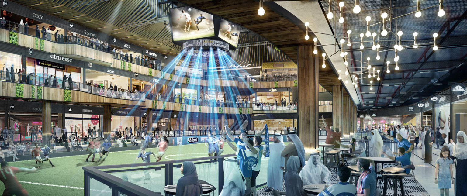 Soccer field in a triple height atrium. Seating on sidelines with tables. Above, walkways on 2nd and 3rd floors with shops