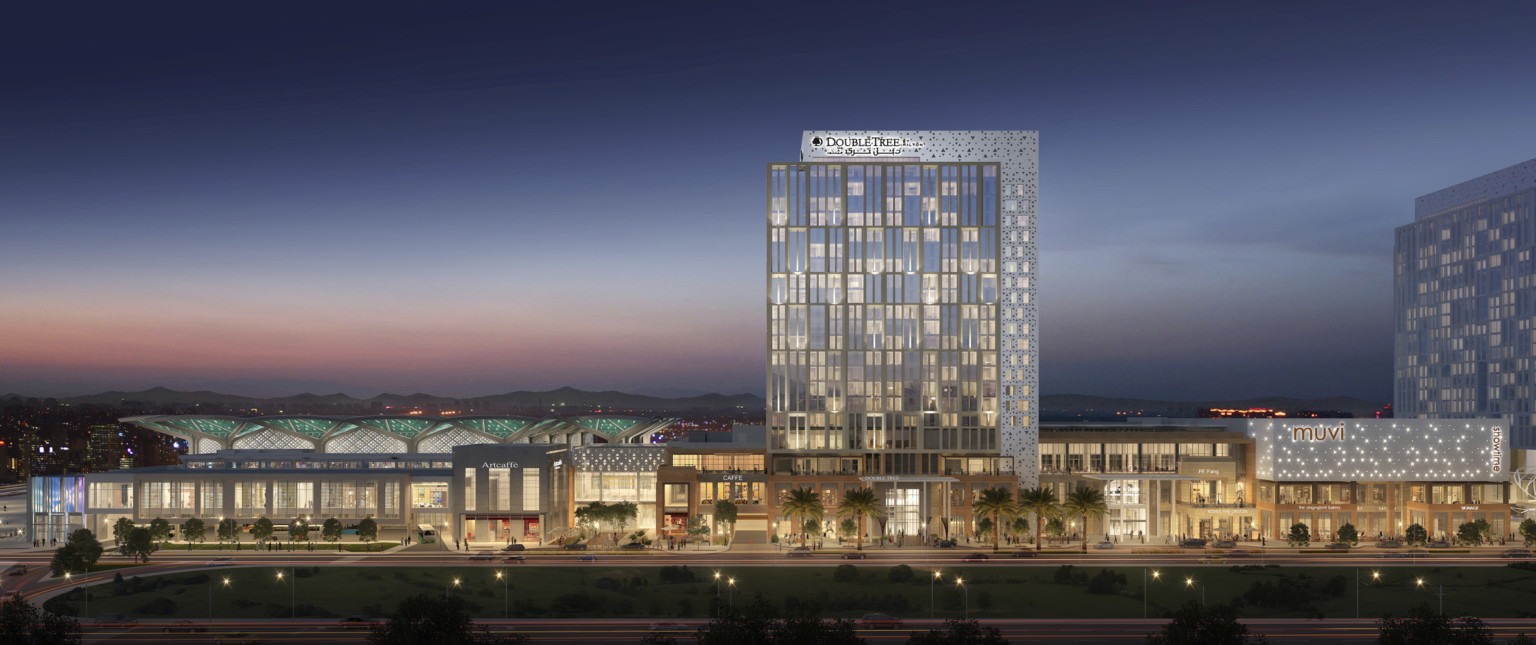 3 story building seen from across parking lot, Double Tree hotel rising above at center. Multiple entrances and large windows