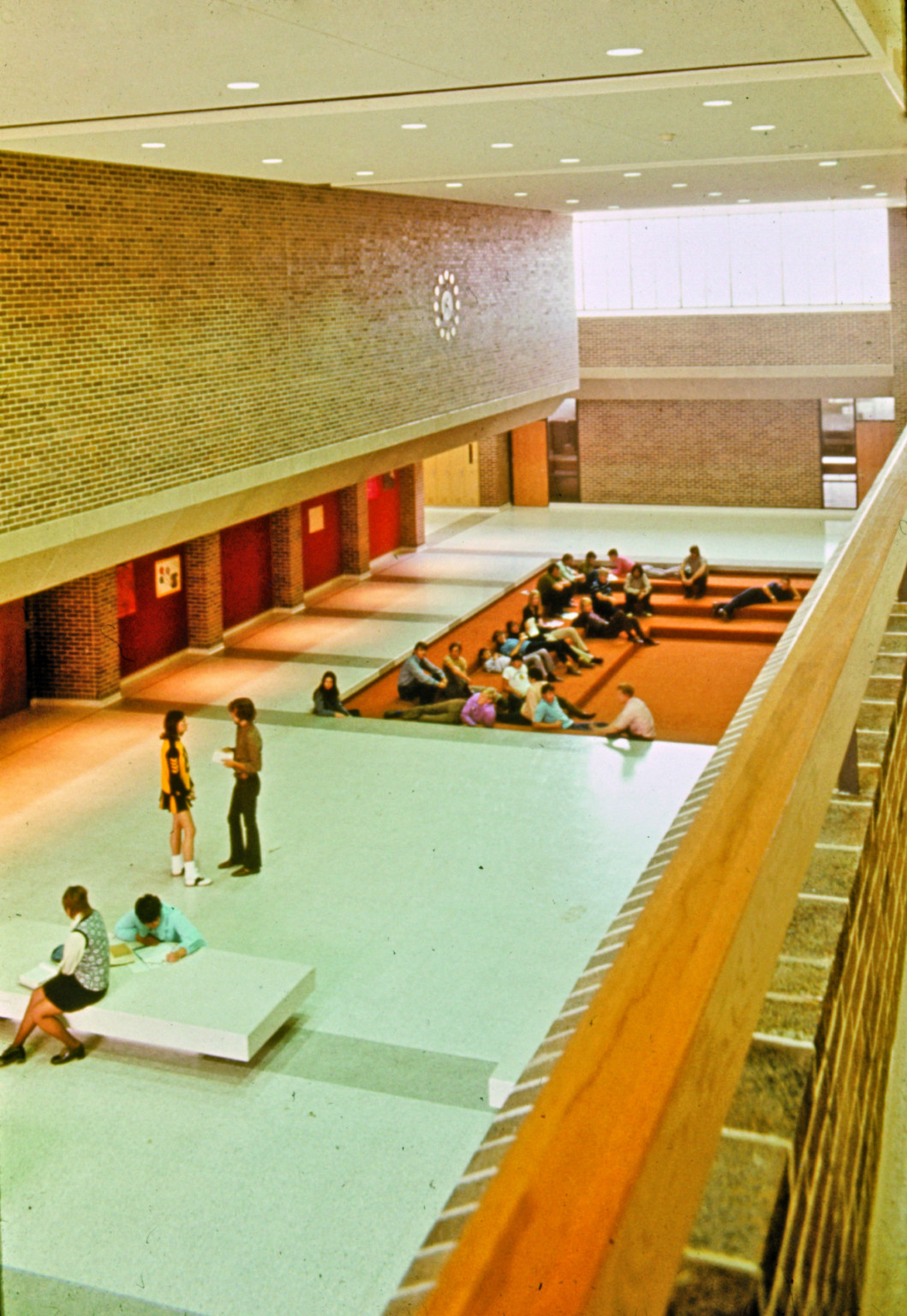 Bryan High School in Omaha, looking down on first floor with red and brick walls. Students gathered in recessed seating area