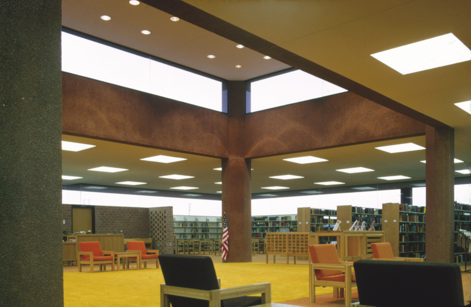 View inside Pierre Public Library, bookshelves to right and seating in center. Clerestory windows let light in from above