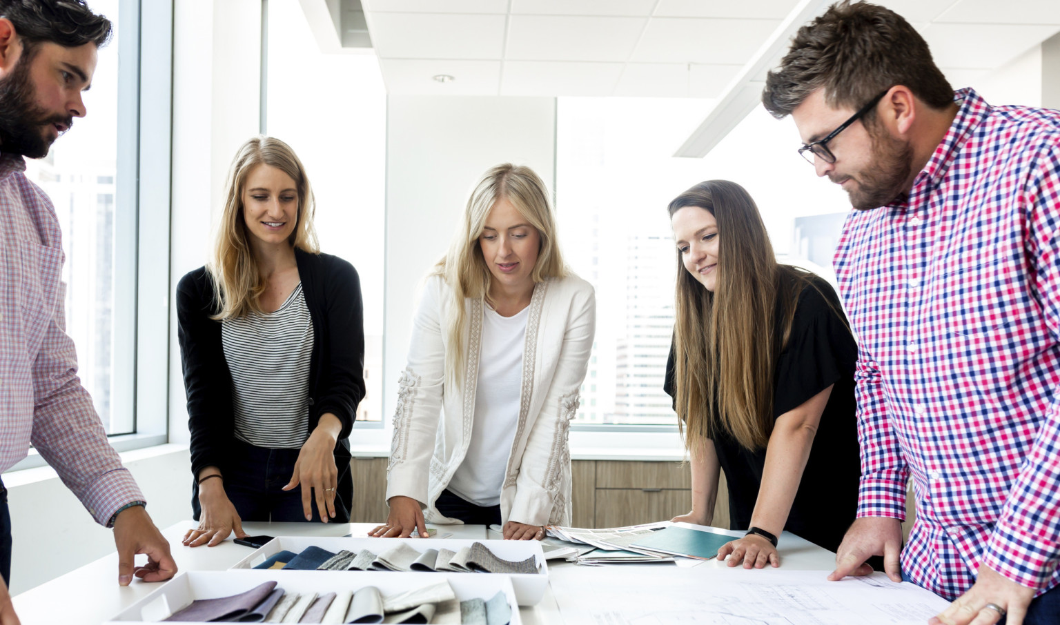 Group of people standing around a table with interior design materials and fabrics Group of people standing around a table with interior design materials and fabrics