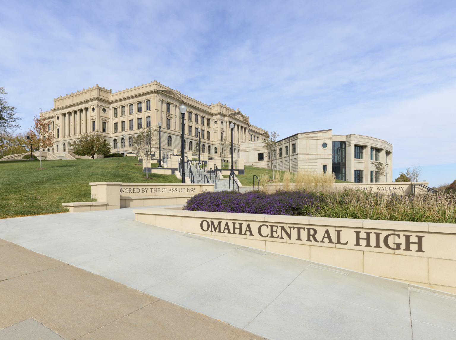 Exterior view of Omaha Central High School, a large 3 story beige stone building with new addition. Garden, front, behind sign