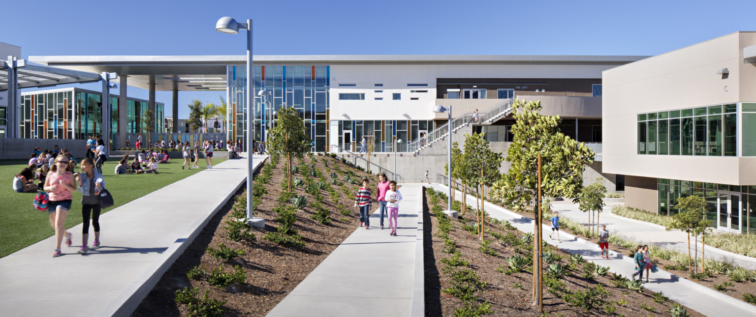 children walking on diagonal concrete paths between landscaping in front of Design 39, a multistory building with glass facade