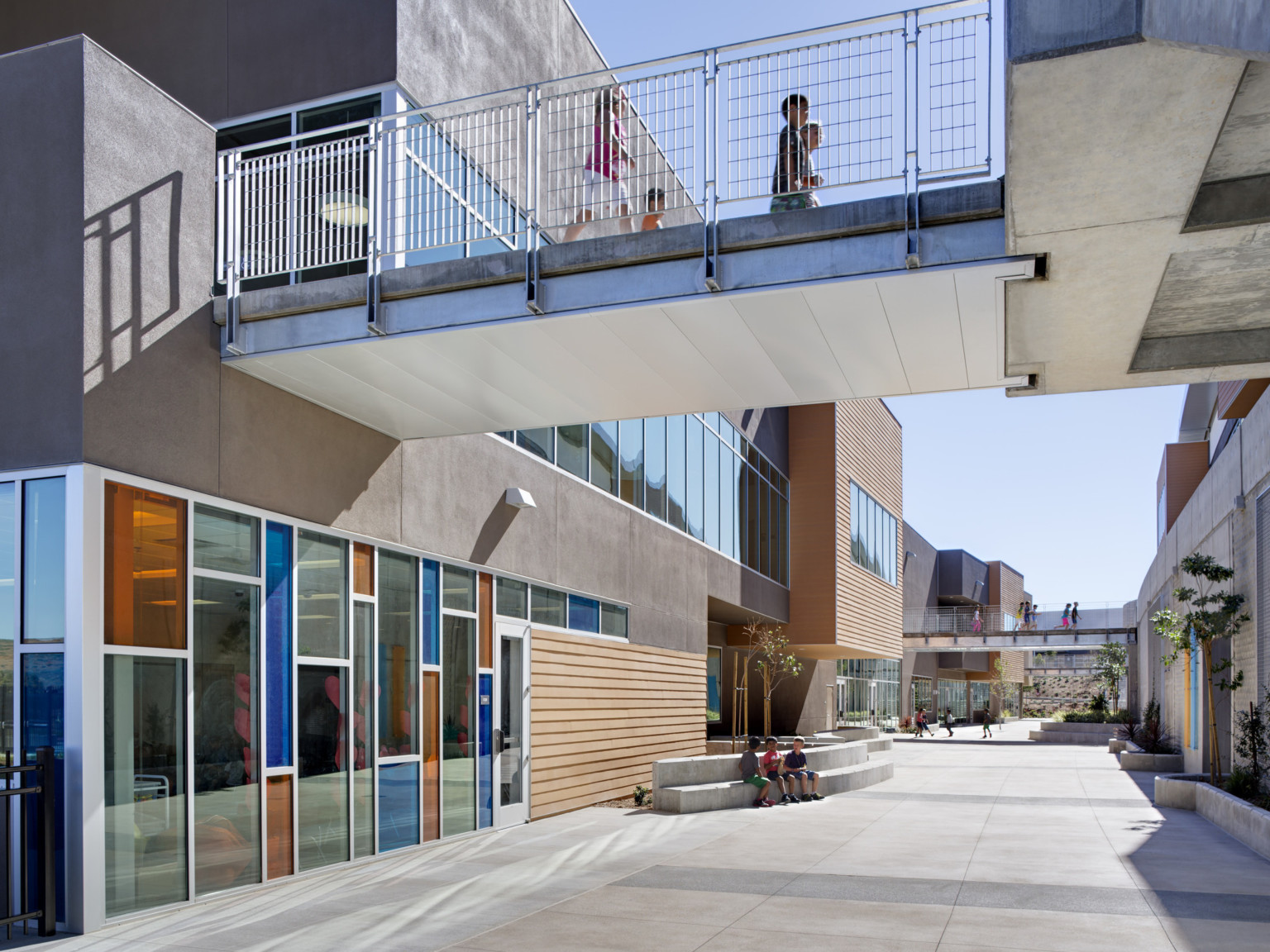 Breezeway between multistory buildings with bridges connecting them. Blue and orange window panes below, wood panel accents