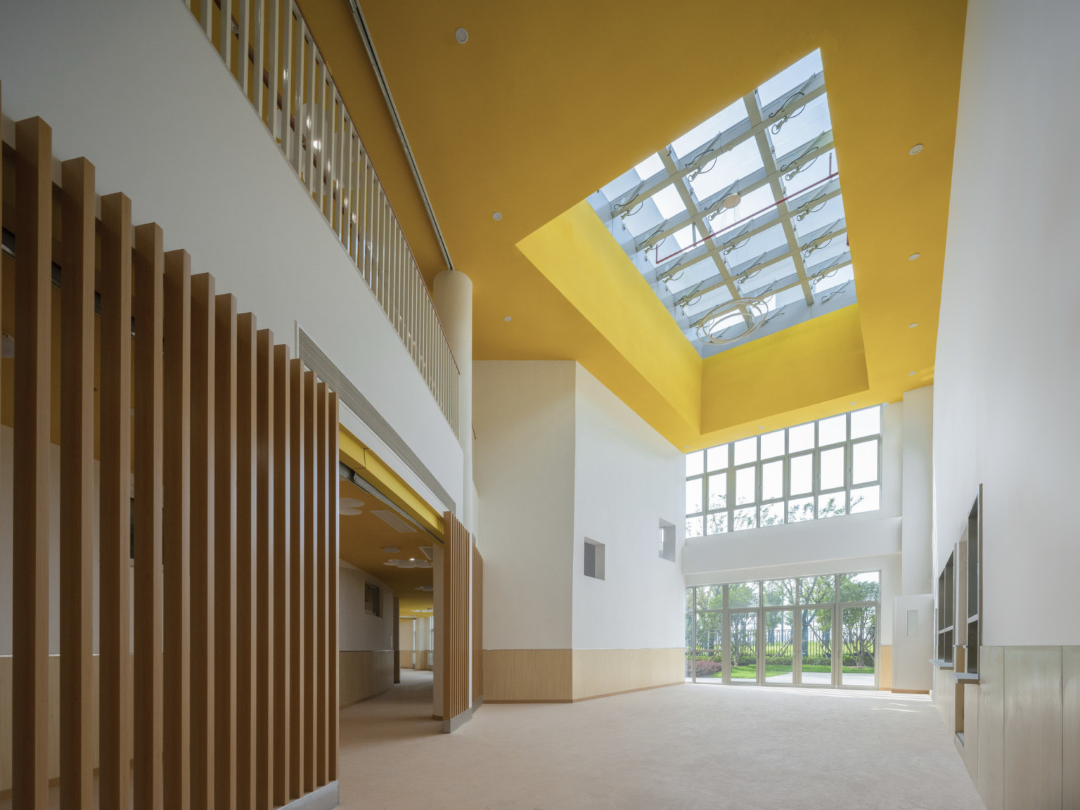 Double height interior hallway with wood slat accents to left and yellow ceiling around skylight, window wall at end of hall