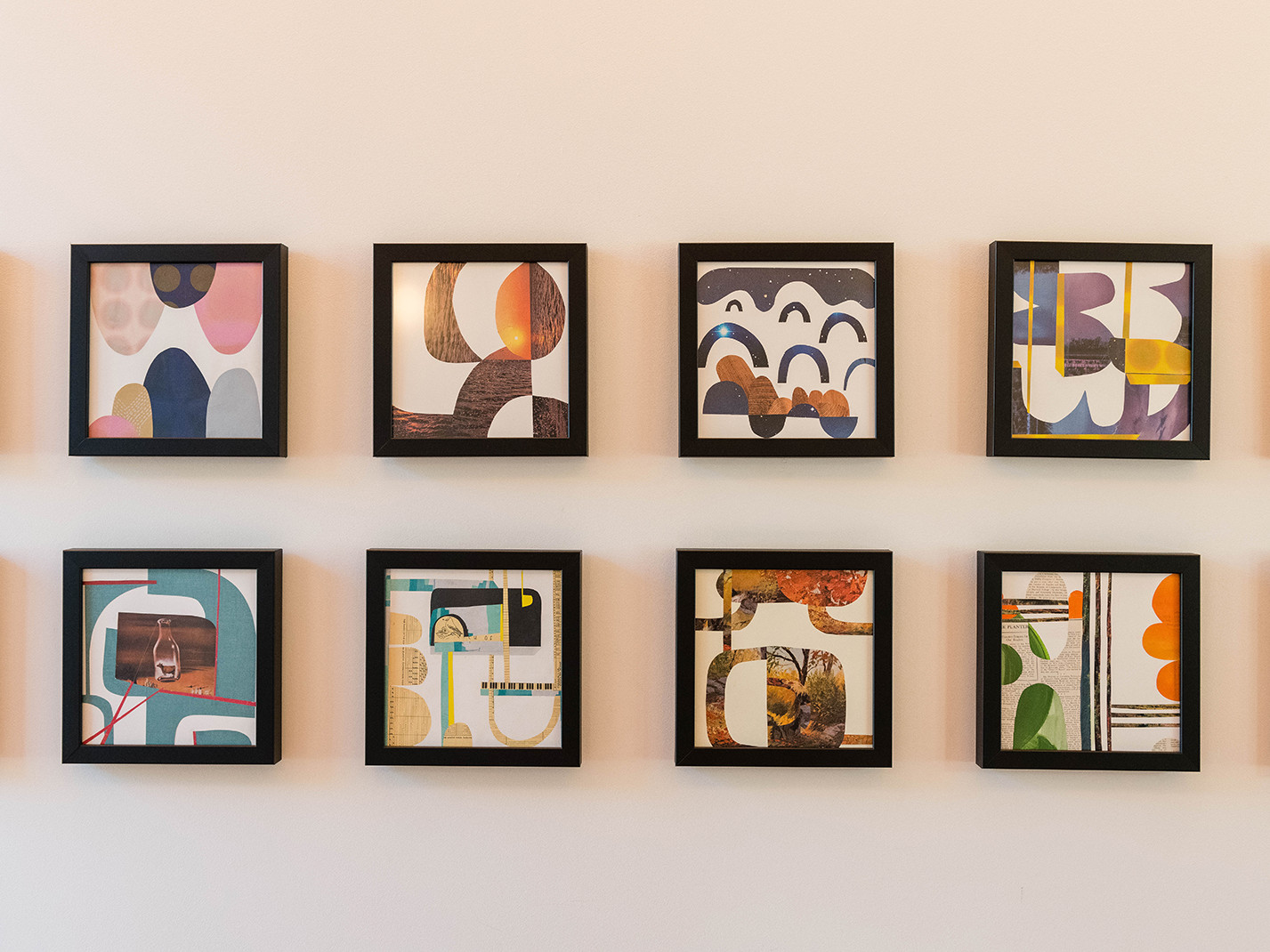 two stacked rows of repeating square black frames on a neutral color wall hold geometric and colorful art prints