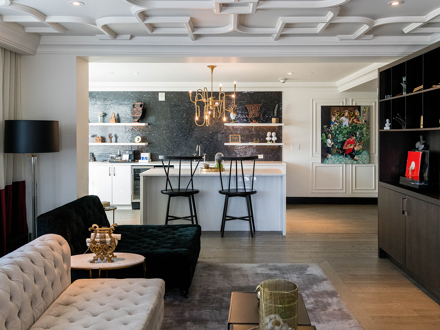 white molding walls and ceiling and oak wood floors with tufted velvet couches. a marble kitchen island with two black stools