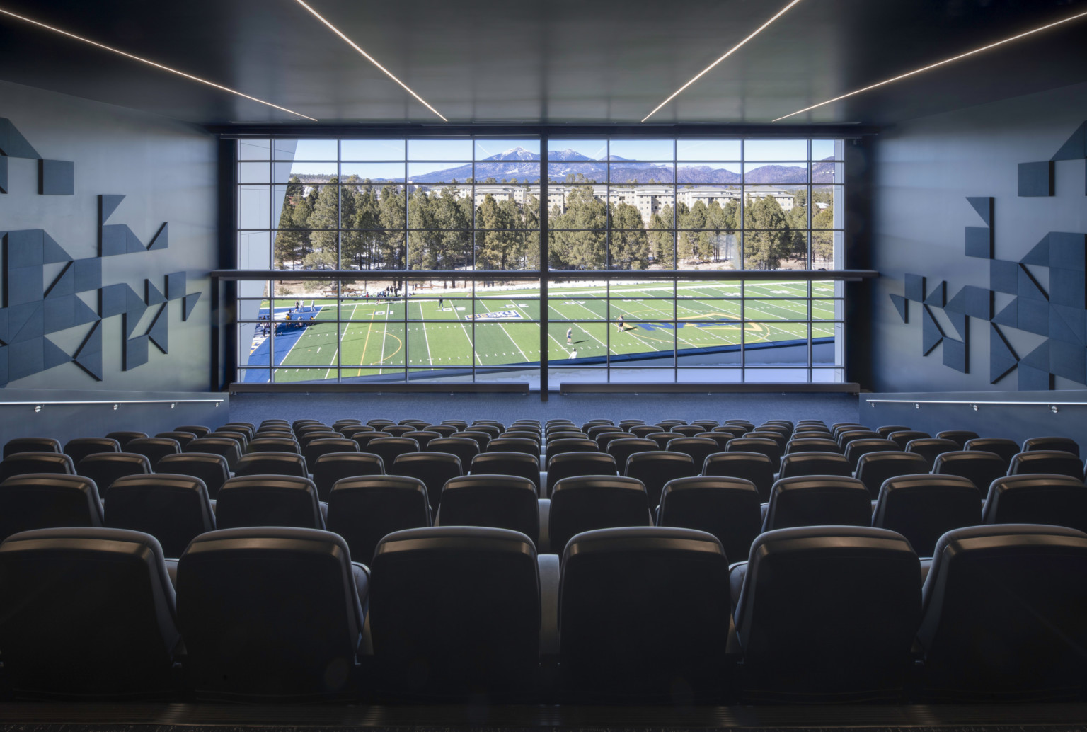 auditorium with square and triangular acoustic panels and glass wall view of playing field, pine trees, and mountain range