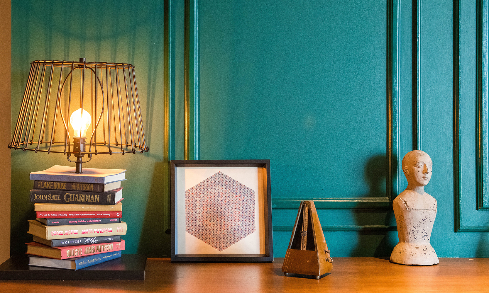 dark green wall with molding details behind a lamp made from stack of books, framed art print vintage metronome and cast bust dark green wall with molding details behind a lamp made from stack of books, framed art print vintage metronome and cast bust