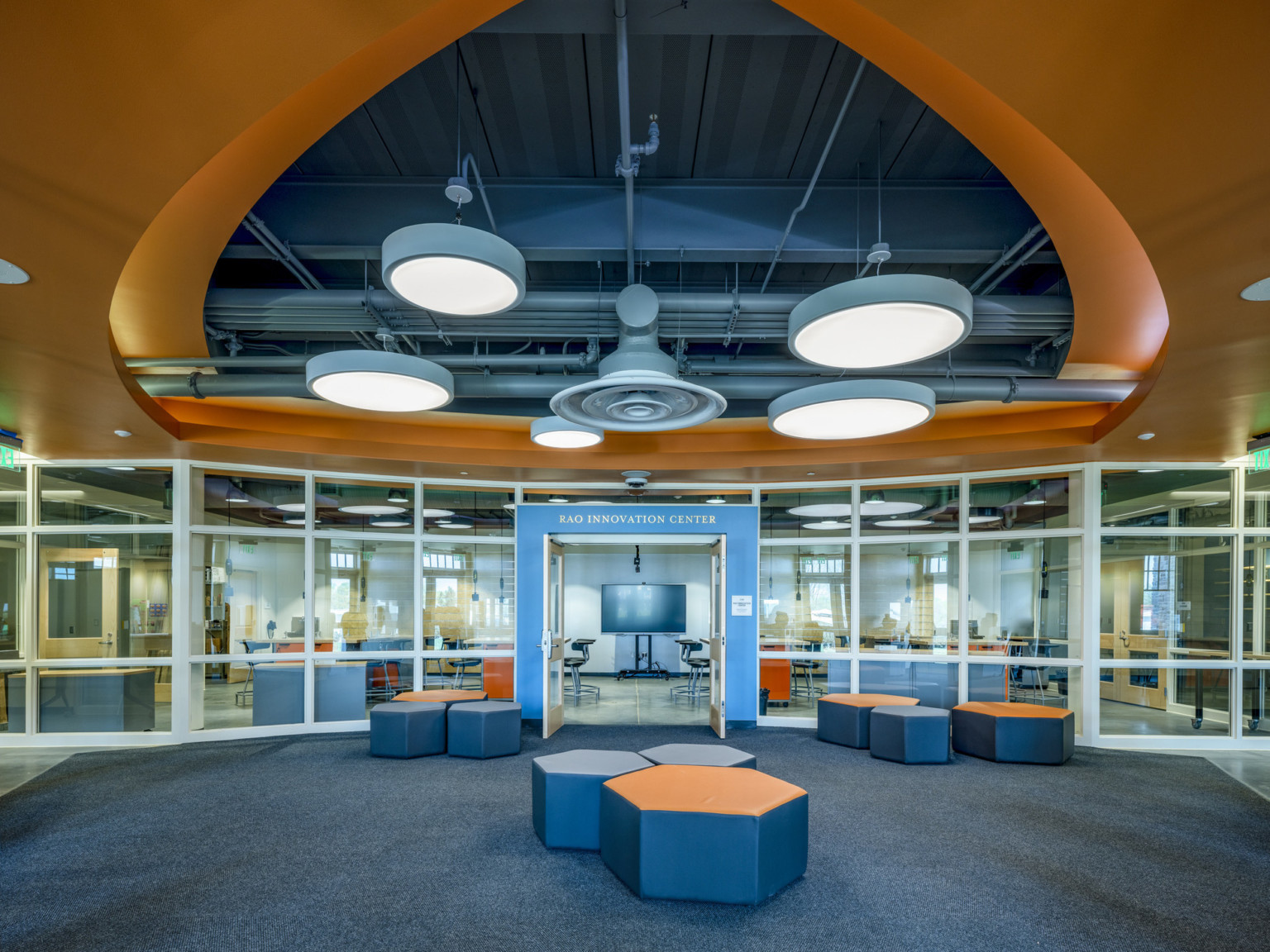 Abstract orange drop ceiling detail with cut out with exposed ducts and round pendant lamps. Flexible seating in common area
