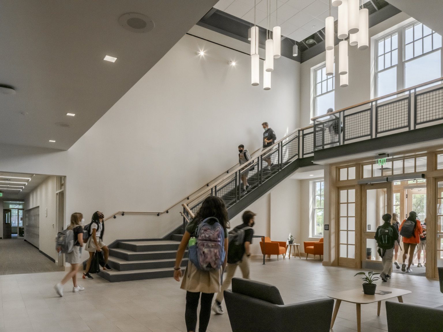 Double height atrium with vertical pendant lights center, stairs wrapping around white room with large windows, hallway left