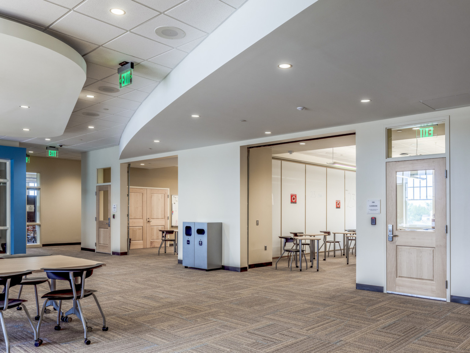 Large open learning space with flexible walls to smaller rooms, rolling chairs and tables throughout. Blue accent wall left