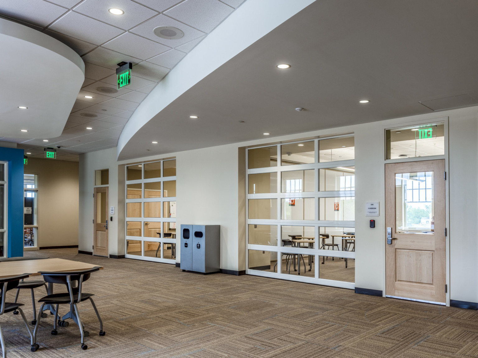 Large open learning space with flexible walls to smaller rooms, rolling chairs and tables throughout. Blue accent wall left