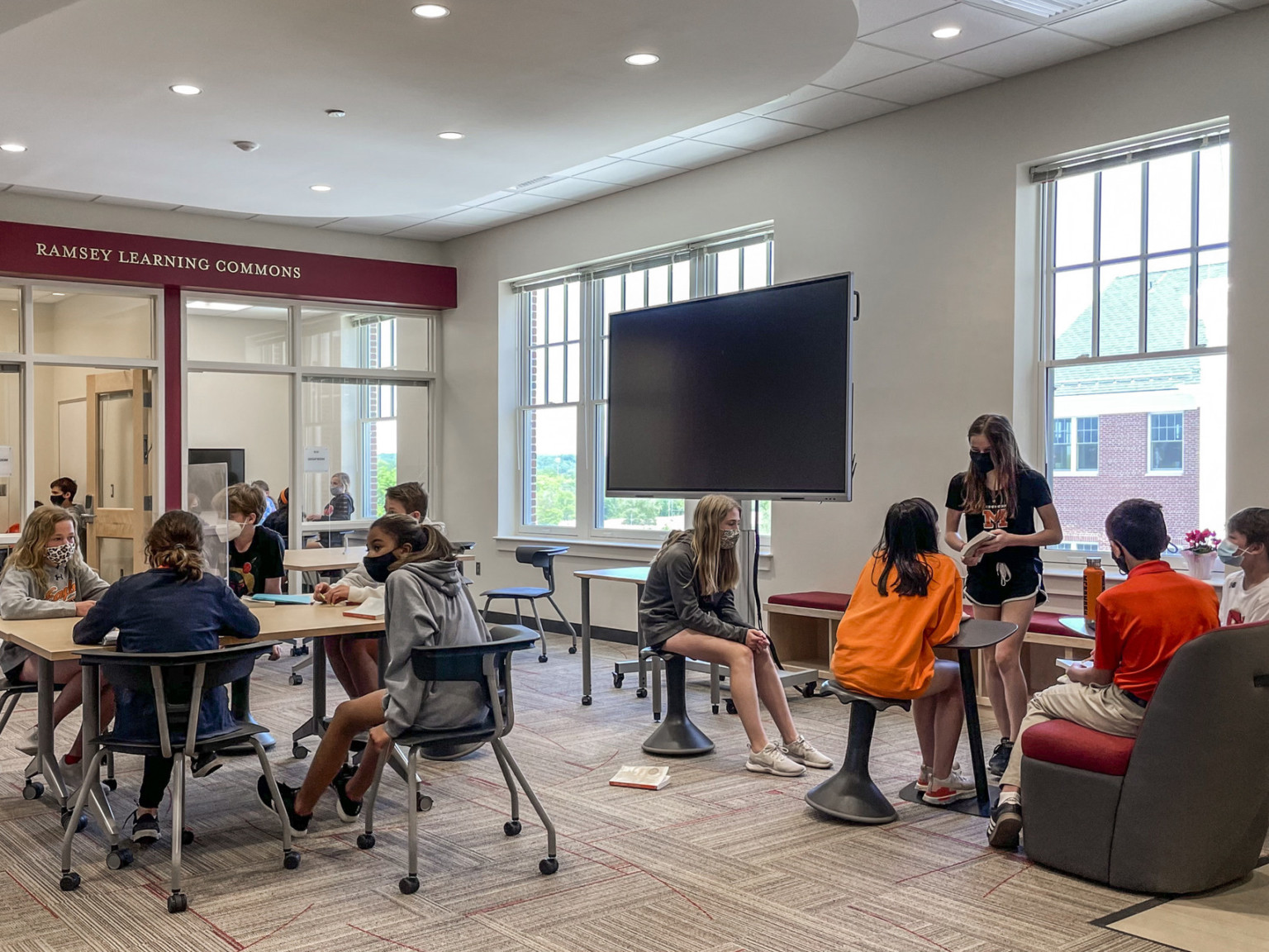 Students in Ramsey Learning Commons, a white room with red accent wall with large interior windows, flexile work space