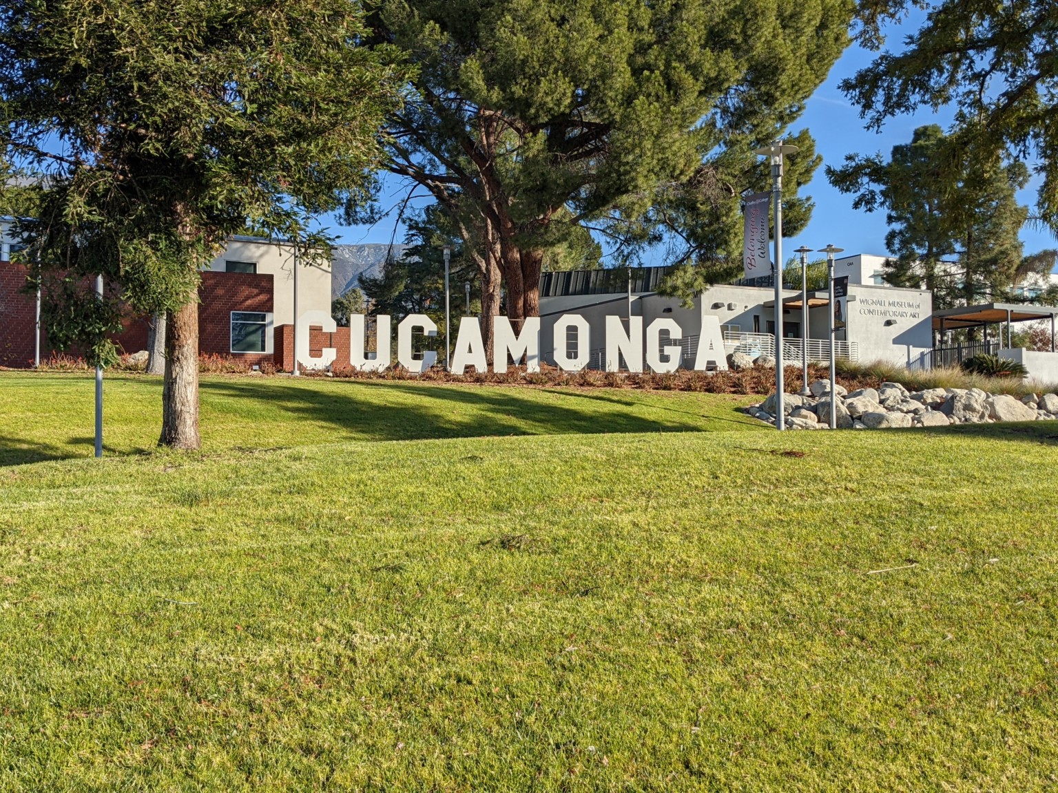 Lowrise beige building at Chaffey College. Rolling grass hill with large letters reading Cucamonga in front of entry