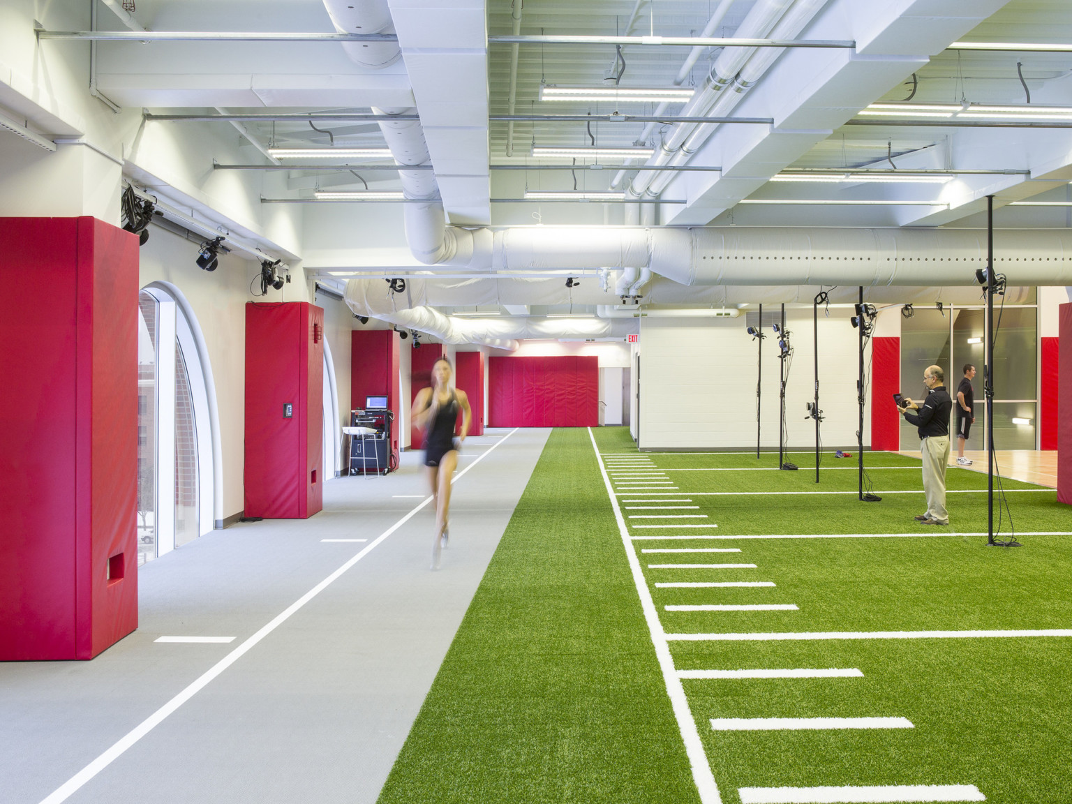 The University of Nebraska Athletic Performance Lab training facility with grey and turf floor in white room with red padding