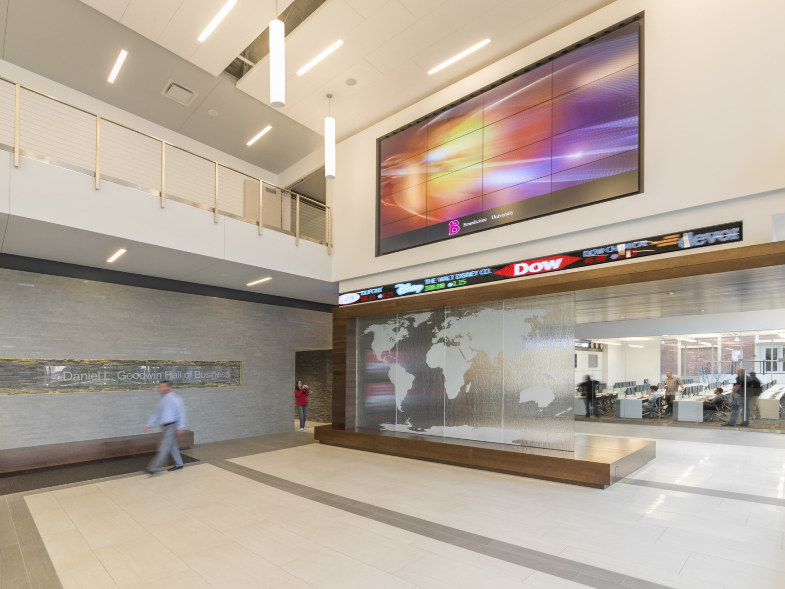 Interior multistory lobby with large screens over stock ticker, glass overlaid with world map. Balcony to left, pendant lights
