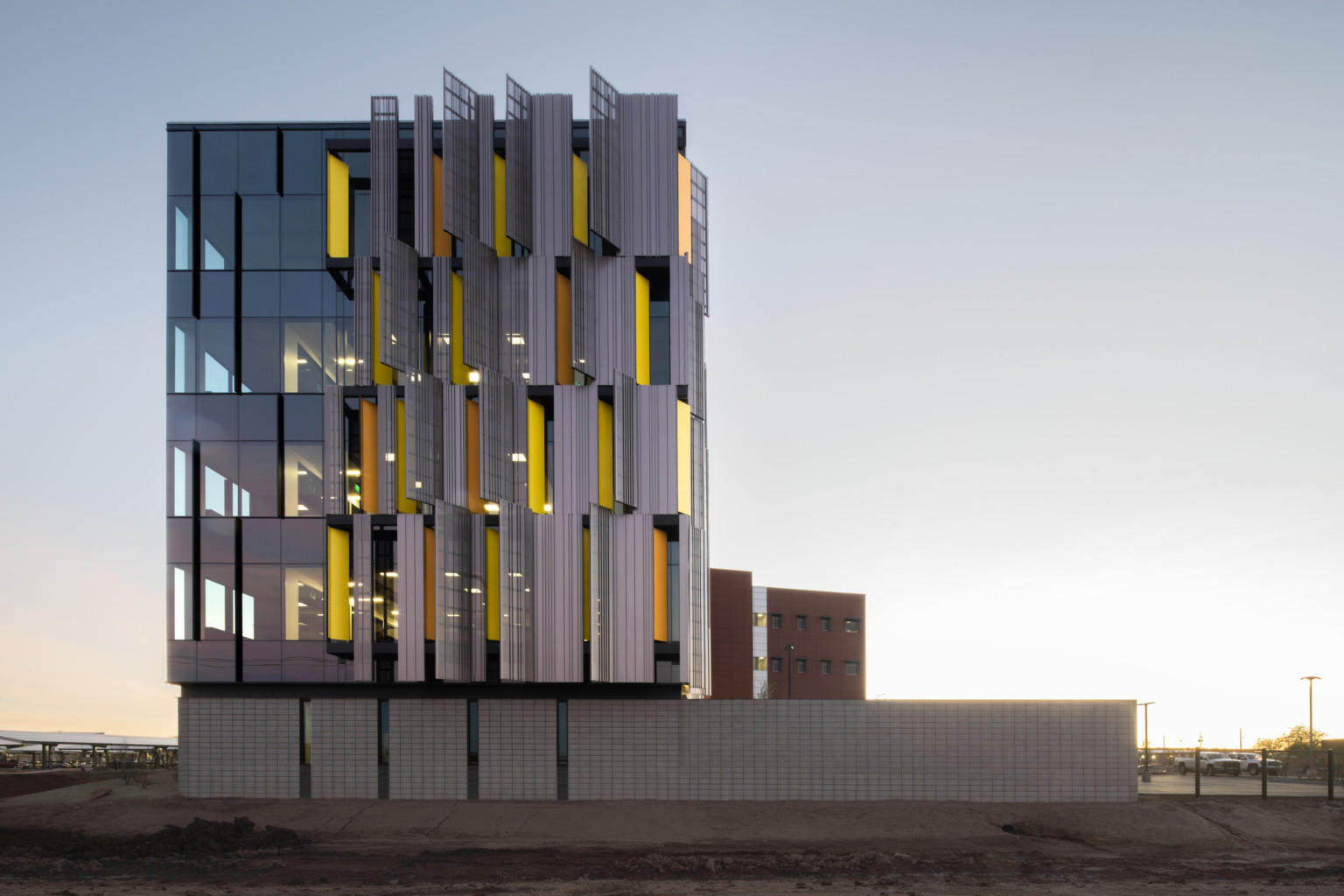 side view of courthouse with serrated sunscreen facade, a pattern of yellow panels peaking between. Floor to ceiling windows