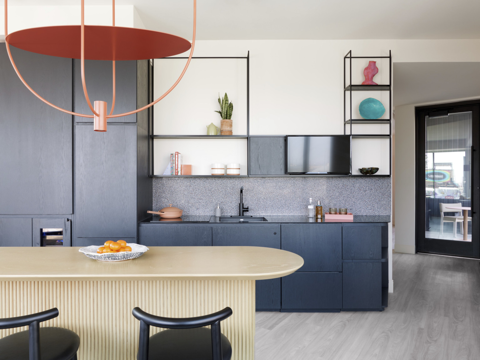 Full kitchen at an extended stay hotel in Denver. Modern orange chandelier hangs over a wood island, black cabinets in the background