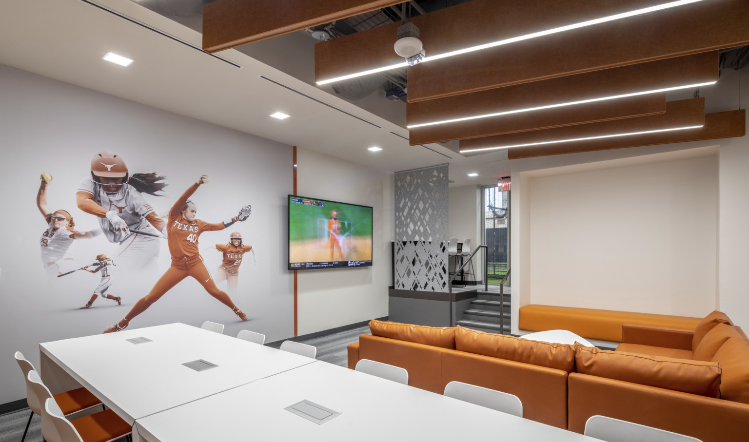 University of Texas Softball Development Facility interior. Softball mural on wall next to screen in front of orange couch