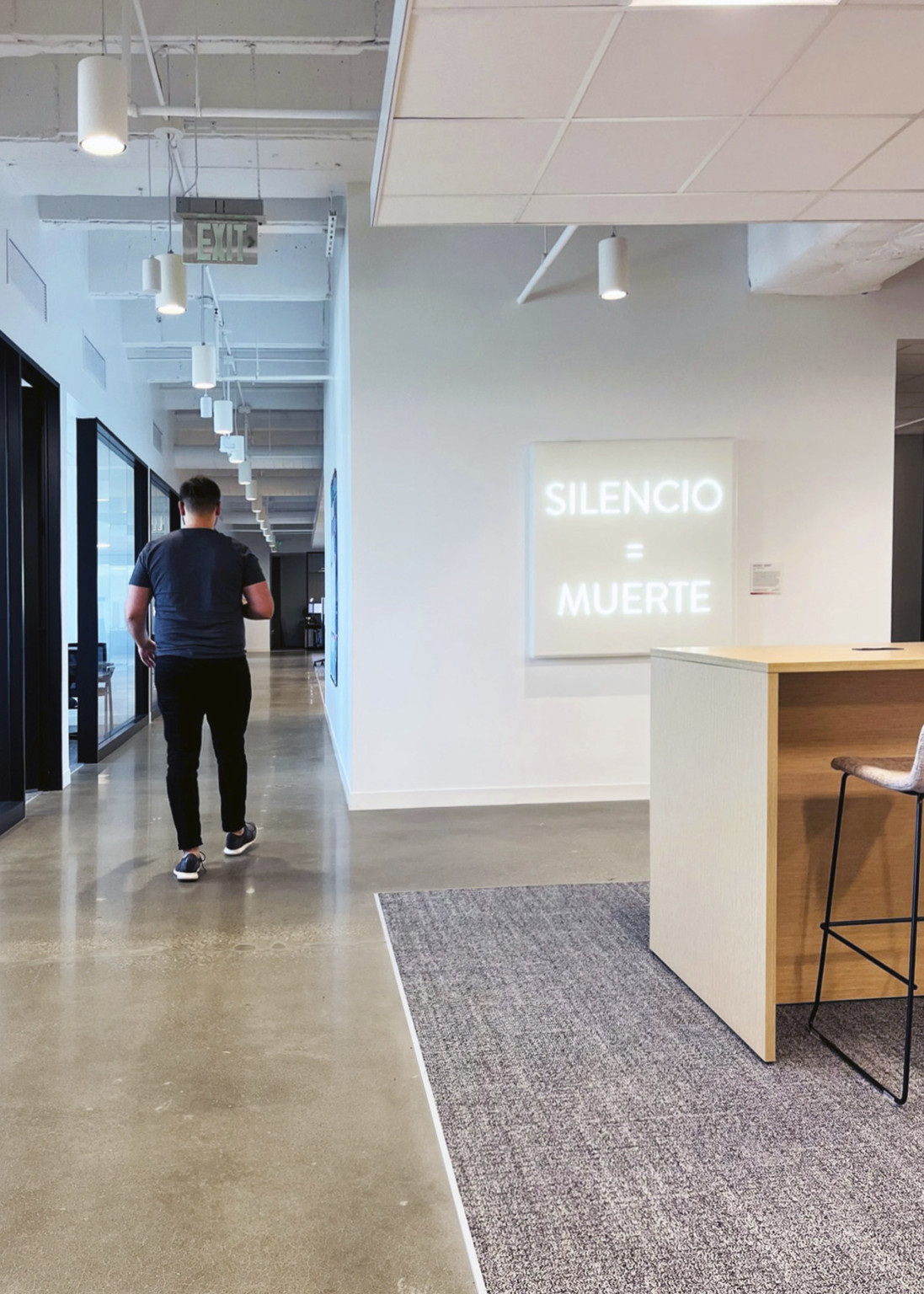man walking down polished concrete floor with gray carpet and white walls with illuminated sign reading silencio = muerte
