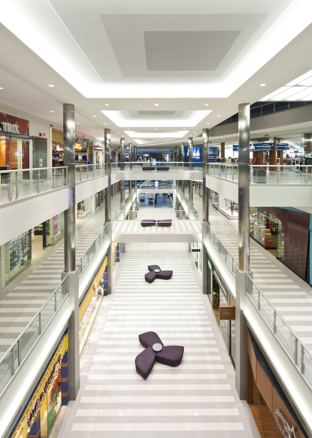 Interior of mall with triple height walkways lined with shops. Purple pinwheel shaped seats down the 1st floor central aisle