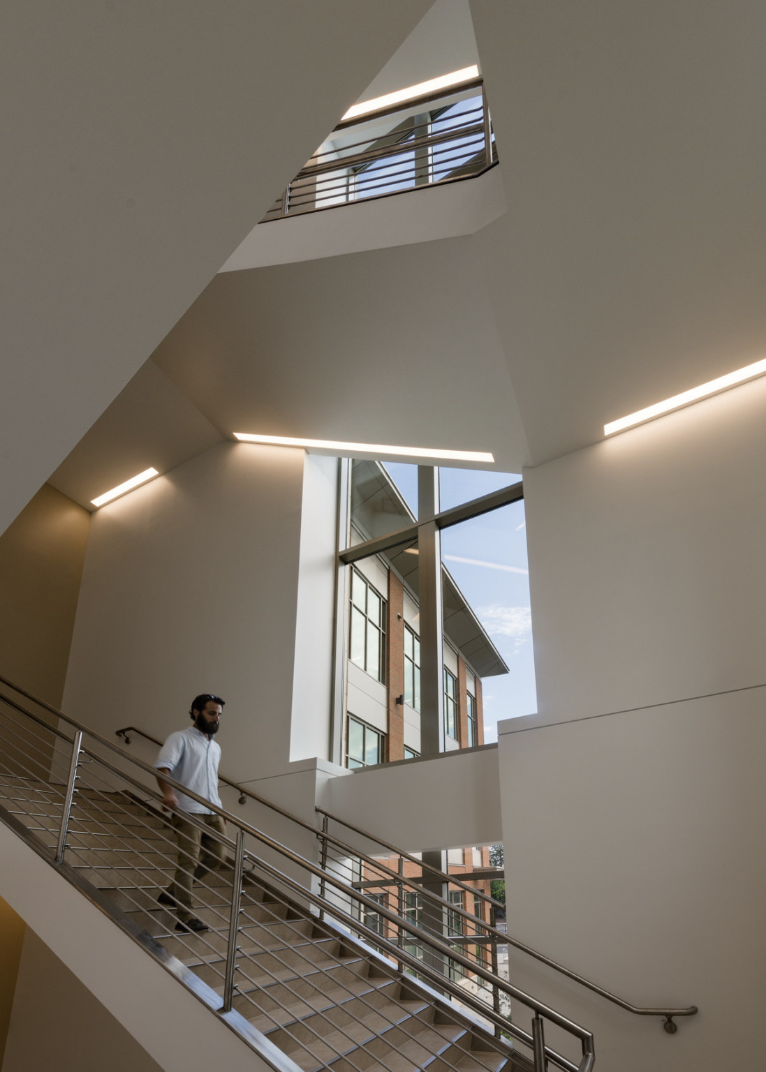 Multistory white open stairwell with light panels wrapping along edge of ceiling. Large windows run down back wall