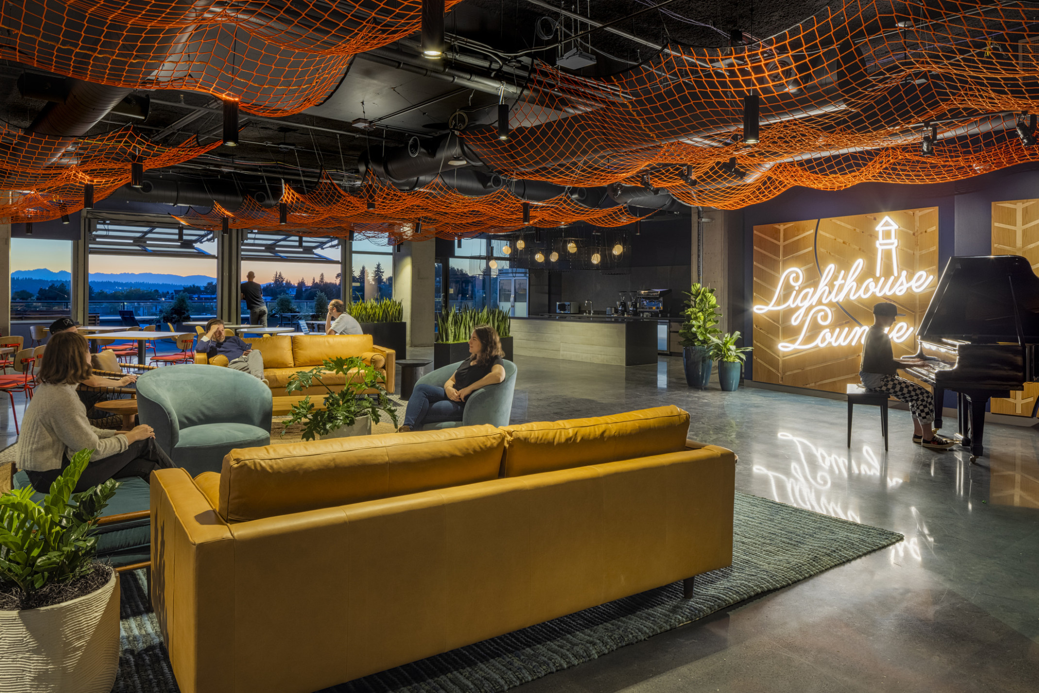workplace lounge with piano and fishing net art installation, garage doors open to mountain views at sunset workplace lounge with piano and fishing net art installation, garage doors open to mountain views at sunset