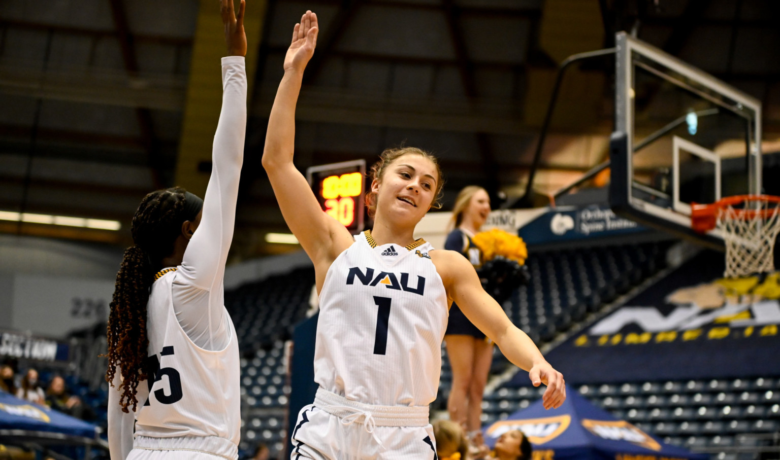 Northern Arizona University female student athlete high fiving during basketball game on court basket upper right Northern Arizona University female student athlete high fiving during basketball game on court basket upper right