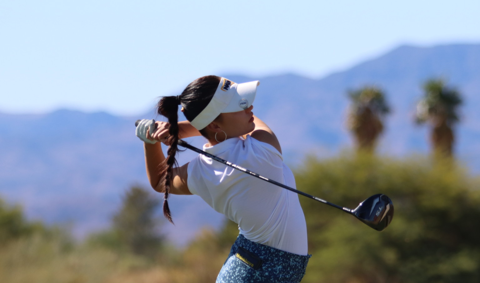 Northern Arizona University female student athlete golfing in desert region in front of mountains