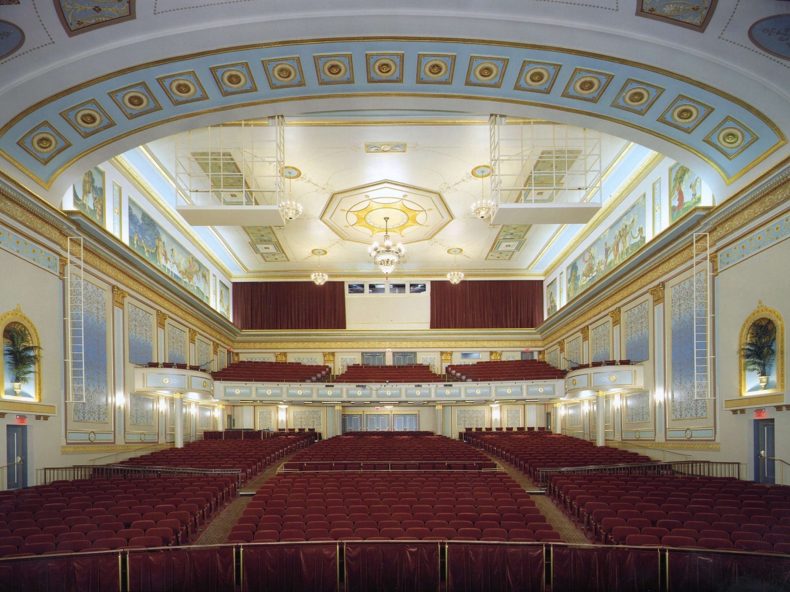 Audience gallery viewed from stage, gold accents on white walls with blue picture frame mouldings, brown seats and balcony