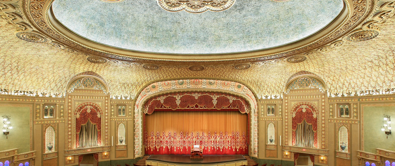 Audience gallery, from balcony looking to stage. Ornate patterned ceiling with round recessed detail illuminated at inner edge