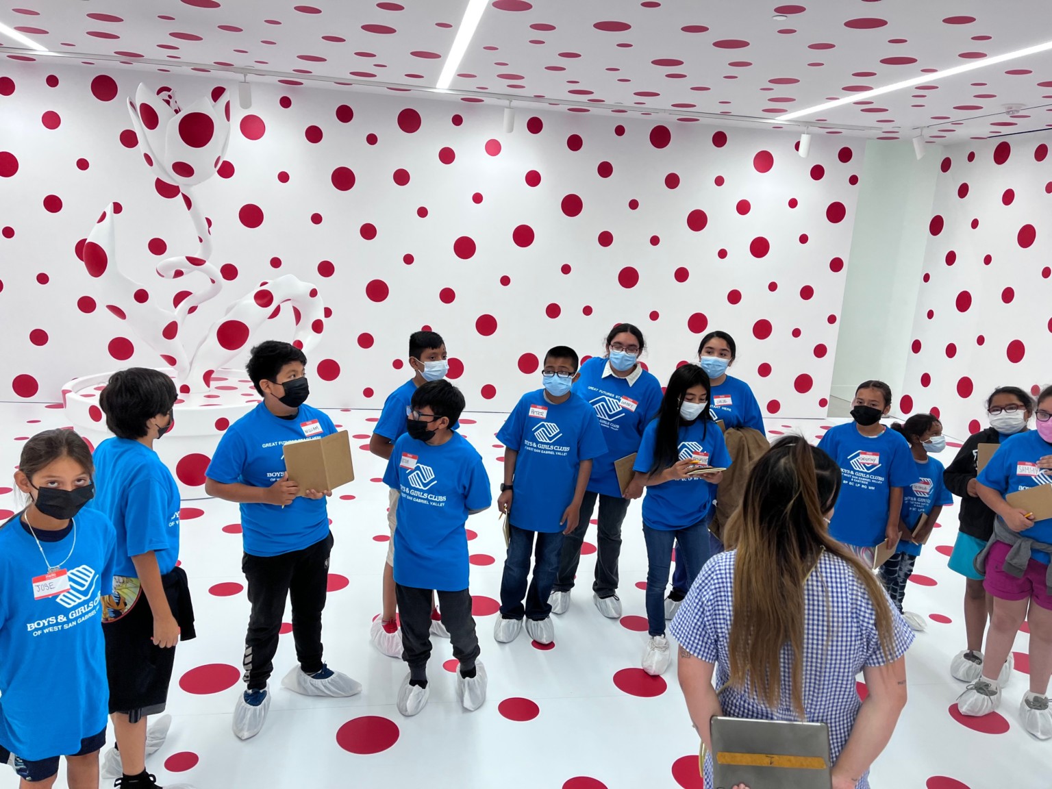 Students standing around inside a museum space with white walls and red polka dots all around