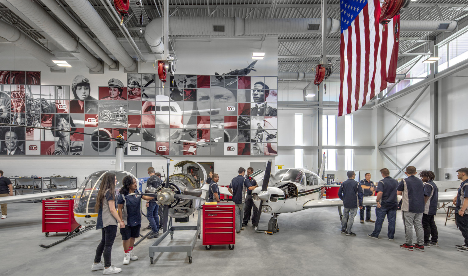 Aviation lab with helicopter, small plane, and displayed engine. Mural at back with planes and pilots. American flag, right Aviation lab with helicopter, small plane, and displayed engine. Mural at back with planes and pilots. American flag, right