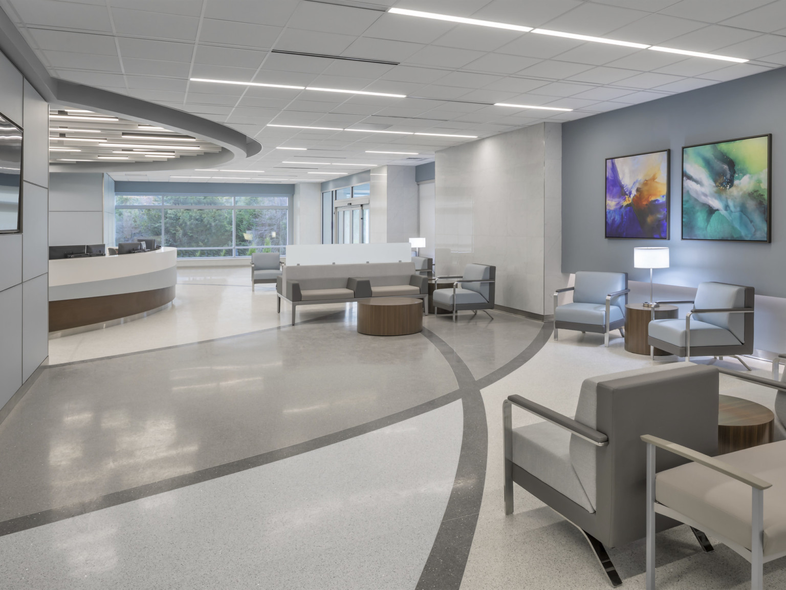 Hospital waiting room lobby with chairs and bench seating. Abstract paintings hang on the grey walls with white accents