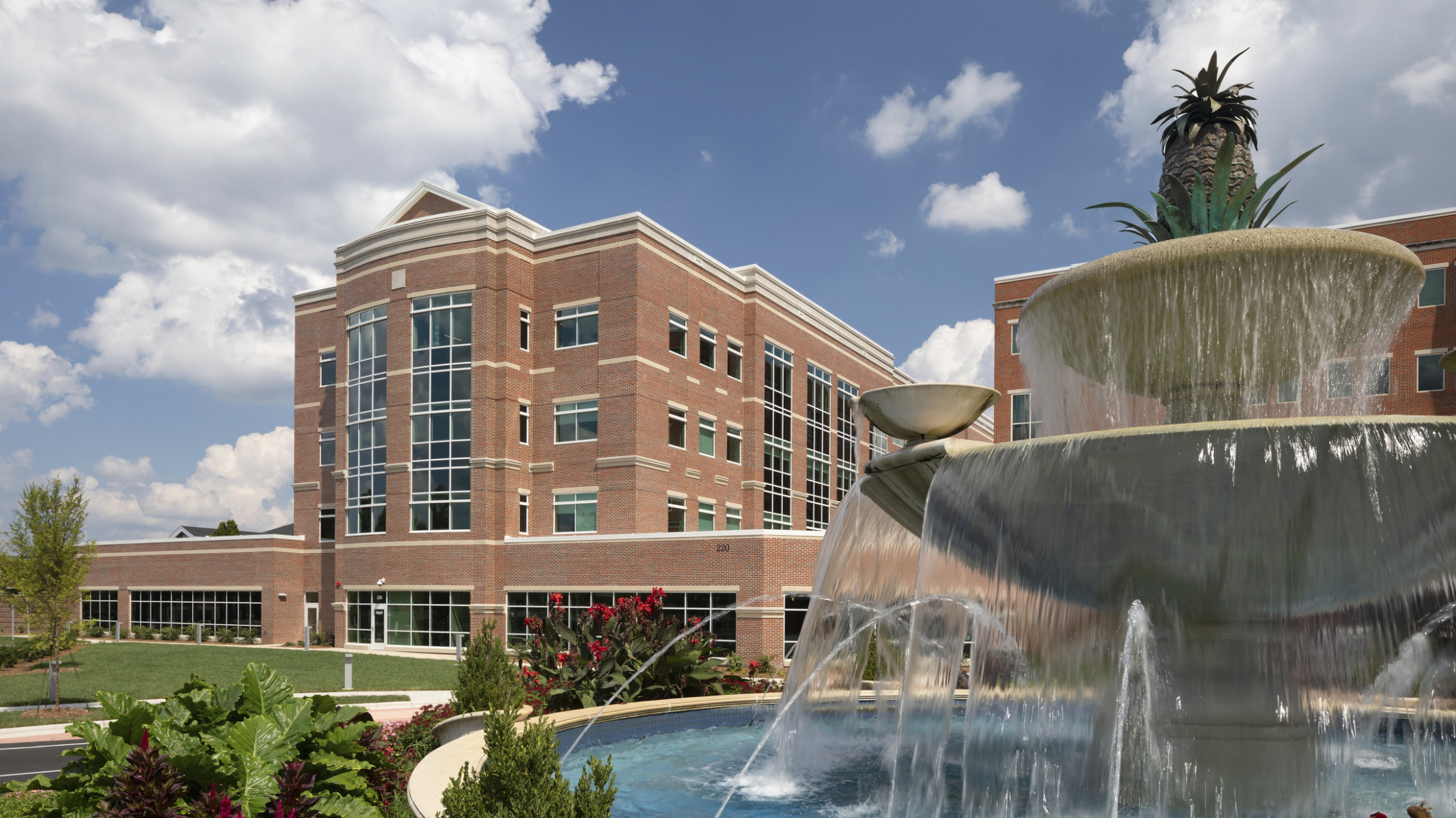 Atrium Health Cabarrus exterior, a brick building with windows along central tower. Landscaped grounds with stepped fountain